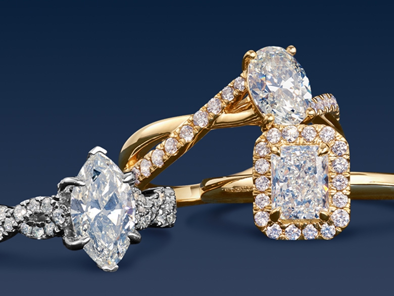 Three engagement rings from the Helzberg Signature Collection stacked on top of each other in front of a dark blue background.